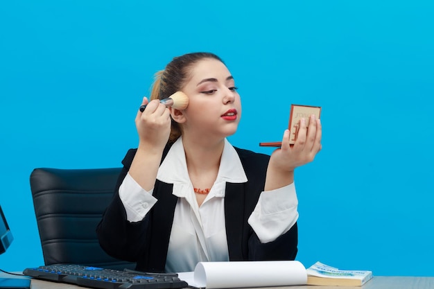 Jonge zakenvrouw die aan de balie zit en make-up op zichzelf aanbrengt