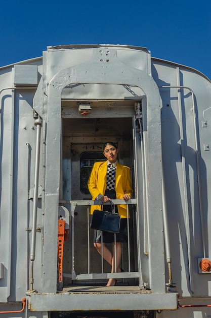 Jonge zakenvrouw die bij de treindeur staat, gekleed in vintage stijl, zwarte rok en gele jas