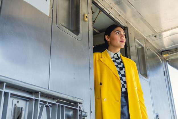 Jonge zakenvrouw die bij de treindeur staat, gekleed in vintage stijl, zwarte rok en gele jas