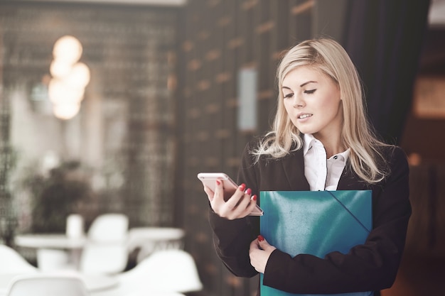 Jonge zakenvrouw die een bericht schrijft op een smartphone en glimlacht op kantoor