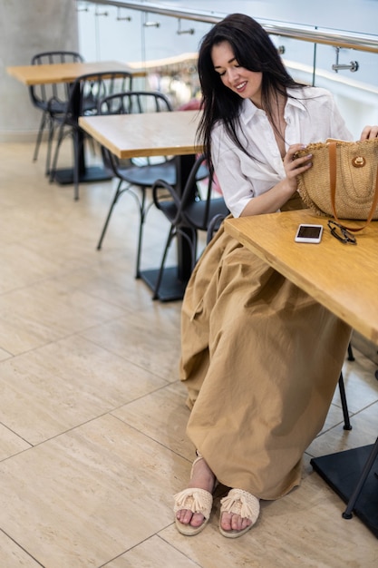 Jonge zakenvrouw die op afstand werkt in een openbare cafetaria die aan het chatten is met een smartphone die aan tafel zit