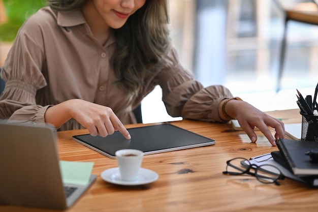 Jonge zakenvrouw die voor een laptopcomputer zit en digitale tablet gebruikt