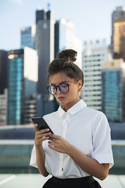 Jonge zakenvrouw gebruikt smartphone in de stad met moderne gebouwen