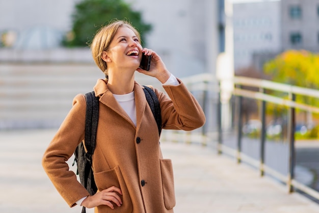 Jonge zakenvrouw glimlachend en lachend op een smartphone oproep universiteitsstudent met mobiele telefoon elegante duizendjarige meisje in de stad concept van vrijheid om te communiceren met nieuwe technologie 5g