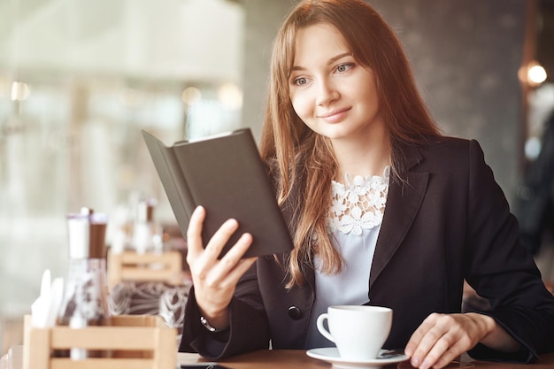 Jonge zakenvrouw in een café die een e-boek leest en koffie drinkt