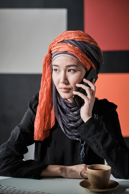 Jonge zakenvrouw in hijab praten op mobiele telefoon tijdens het werken op haar werkplek op kantoor