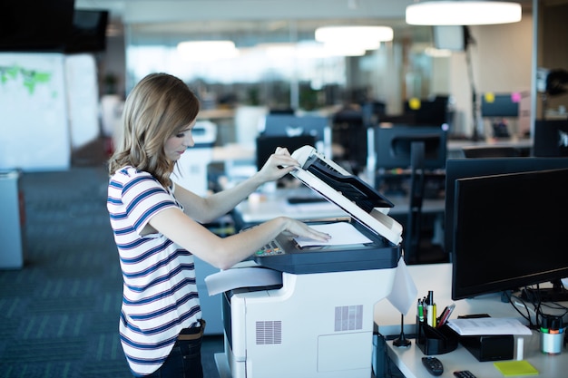 Jonge zakenvrouw met behulp van kopieermachine in kantoor