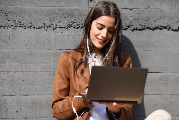 Jonge zakenvrouw met een laptop terwijl ze tegen de muur zit