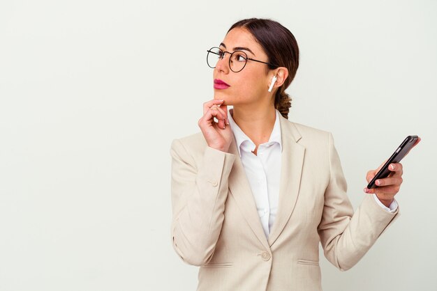 Jonge zakenvrouw met een mobiele telefoon geïsoleerd op wit zijwaarts kijkend met twijfelachtige en sceptische uitdrukking.