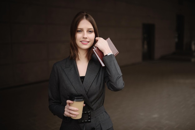 Jonge zakenvrouw met een notitieboekje en koffie op straat