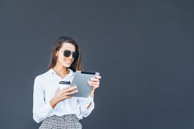 Jonge zakenvrouw met koffie en tablet op grijze achtergrond.