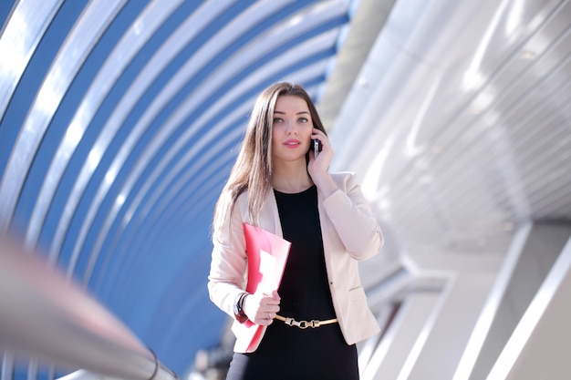 Jonge zakenvrouw met map praten aan de telefoon in modern gebouw