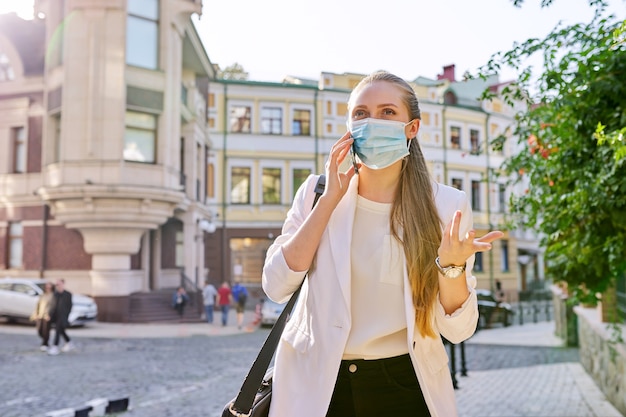 Jonge zakenvrouw met medisch beschermend masker praten op smartphone buitenshuis, stad straat achtergrond. Zaken, pandemie, epidemie, gezondheidszorg en geneeskunde, gezonde levensstijl