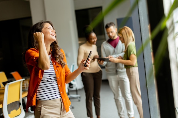 Jonge zakenvrouw met mobiele telefoon voor haar team op het moderne kantoor