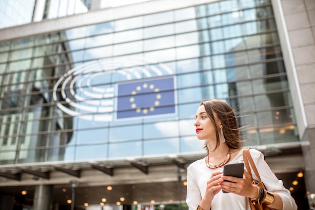 Jonge zakenvrouw permanent met telefoon in de buurt van het Parlementsgebouw van de Europese Unie in Brussel stad