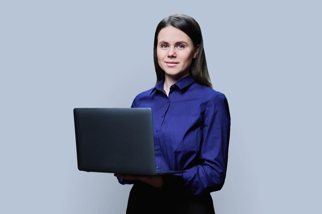 Jonge zakenvrouw poseert met een laptop op een grijze achtergrond