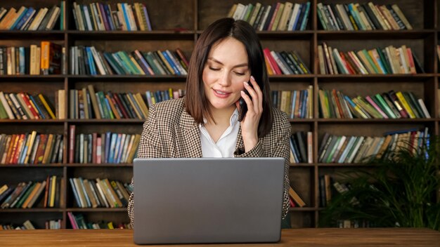 Jonge zakenvrouw praat op zwarte telefoon in bibliotheekhal