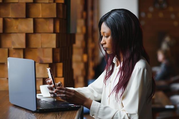 Jonge zakenvrouw regelt de volgende zakelijke bijeenkomst in een moderne coworking-ruimte met behulp van een laptop jonge freelancer-vrouw leest e-mails en andere berichten op een mobiele telefoon