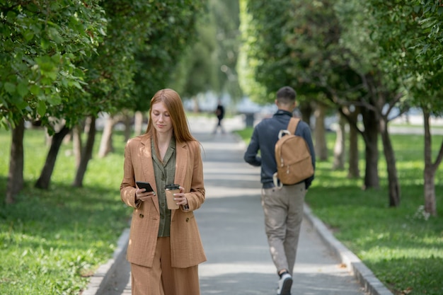 Jonge zakenvrouw scrollen in smartphone tijdens het verplaatsen langs park