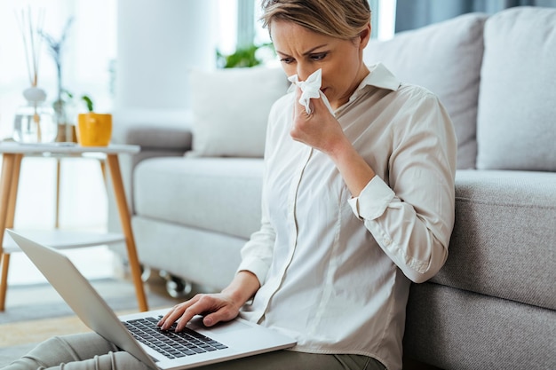 Jonge zakenvrouw snuit een neus terwijl ze thuis aan een laptop werkt