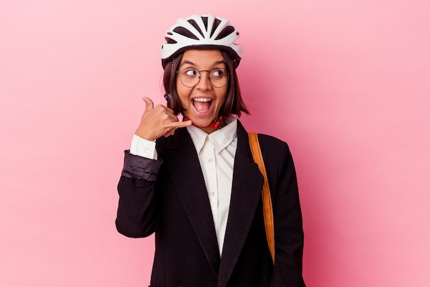 Jonge zakenvrouw van gemengd ras die een fietshelm draagt die op roze achtergrond wordt geïsoleerd en die een mobiel telefoongebaar met vingers toont.