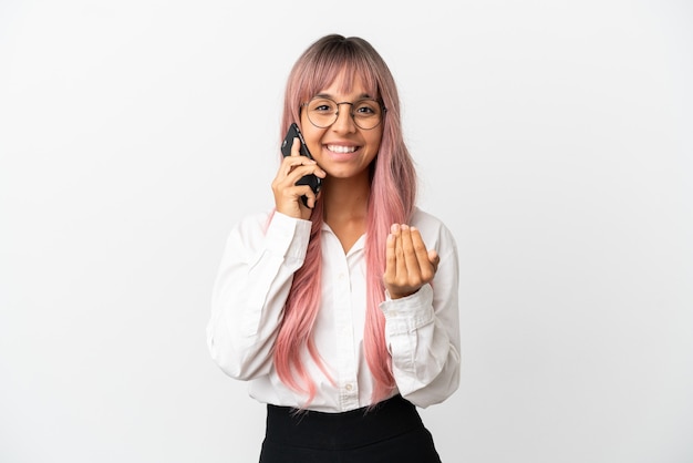 Jonge zakenvrouw van gemengd ras met roze haar met een mobiel geïsoleerd op een roze achtergrond die uitnodigt om met de hand te komen. Blij dat je gekomen bent