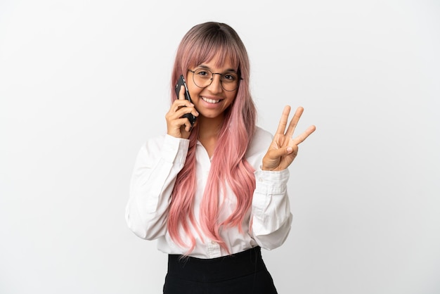 Jonge zakenvrouw van gemengd ras met roze haar met een mobiel geïsoleerd op een roze achtergrond gelukkig en drie tellen met vingers