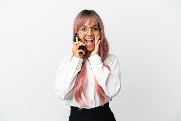 Jonge zakenvrouw van gemengd ras met roze haar met een mobiel geïsoleerd op een roze achtergrond met verrassing en geschokte gezichtsuitdrukking