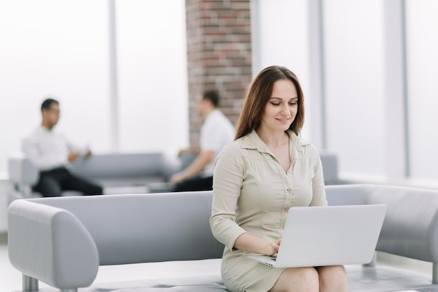 Jonge zakenvrouw zittend op de bank en werken met laptop