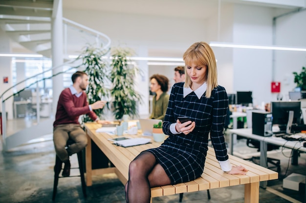 Jonge zakenvrouw zittend op de tafel met een mobiele telefoon