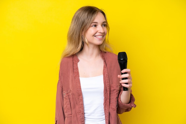 Jonge zanger blanke vrouw die een microfoon oppakt die op gele achtergrond wordt geïsoleerd die kant kijkt