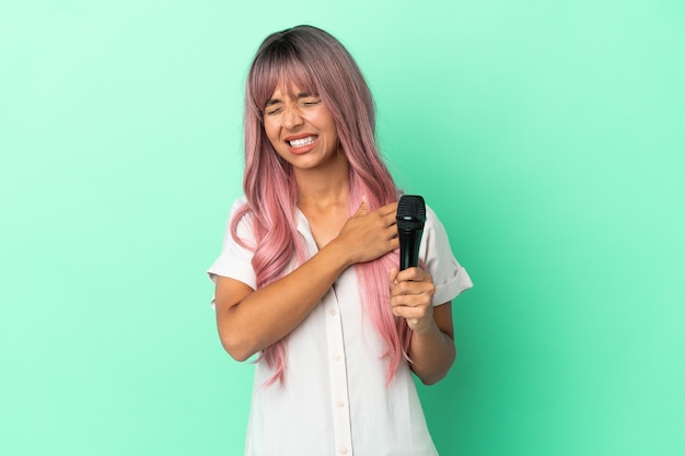 Jonge zangeres van gemengd ras met roze haar geïsoleerd op een groene achtergrond die lijdt aan pijn in de schouder omdat ze moeite heeft gedaan
