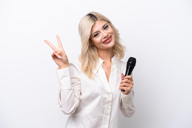 Jonge zangeres vrouw oppakken van een microfoon geïsoleerd op een witte achtergrond glimlachend en overwinning teken tonen