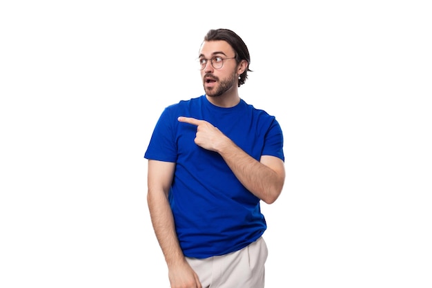 Jonge zelfverzekerde brunette man met een baard gekleed in een blauw T-shirt toont zijn hand naar de ruimte voor