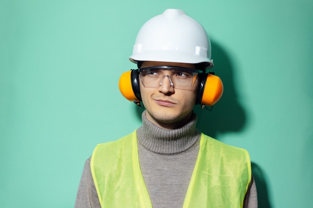 jonge zelfverzekerde ingenieur veiligheidsuitrusting dragen op muur van aqua menthe kleur.