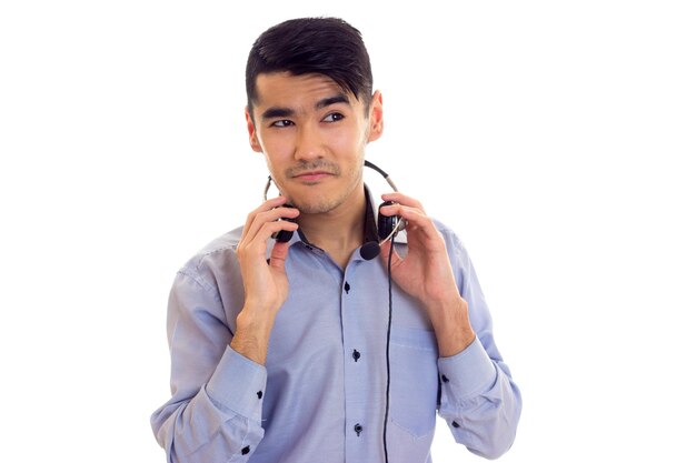 Jonge zelfverzekerde man met donker haar in blauw shirt met zwarte koptelefoon op witte achtergrond in studio