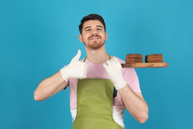 Jonge zelfverzekerde man met verse zelfgemaakte cakeplakken in een blauw.