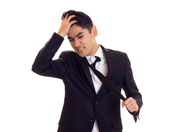 Jonge zelfverzekerde man met zwart haar in wit overhemd en zwarte smoking die zijn zwarte stropdas op een witte achtergrond bevestigt