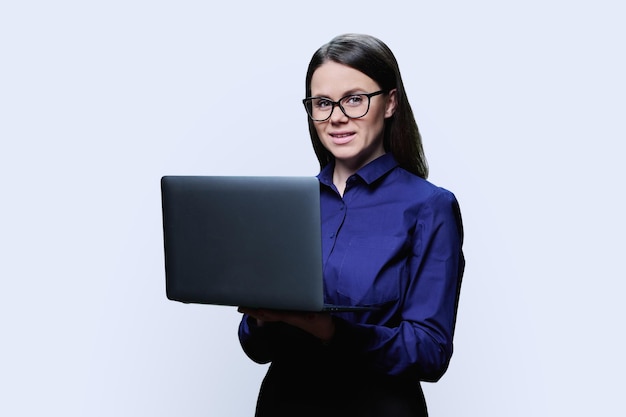Jonge, zelfverzekerde vrouw met een laptop in de hand op een witte achtergrond in een studio glimlachende vrouw in een donker shirt die naar de camera kijkt werk, zaken, onderwijs, digitale internettechnologie mensen