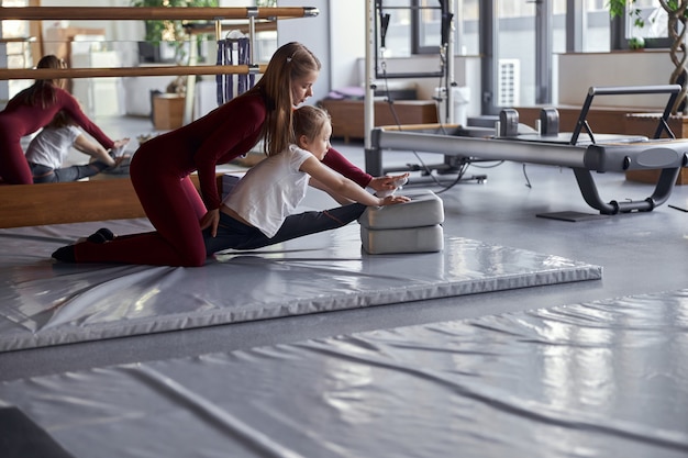 Jonge zelfverzekerde vrouwelijke leraar meisje helpen met het uitrekken in de moderne zaal