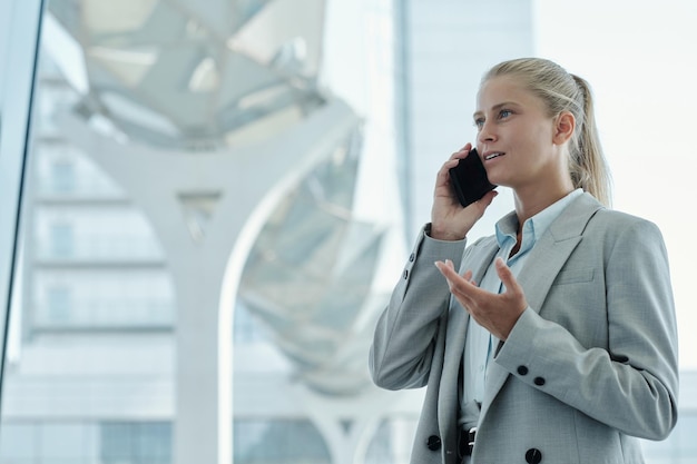 Jonge zelfverzekerde vrouwelijke manager in formalwear die iets aan de telefoon uitlegt