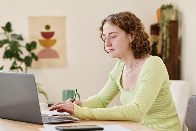 Jonge zelfverzekerde zakenvrouw die aantekeningen maakt terwijl ze voor de laptop werkt