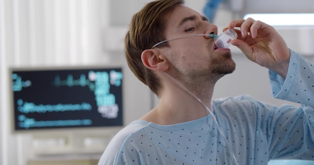 Jonge zieke man die een glas water vasthoudt en een pil neemt in het ziekenhuis
