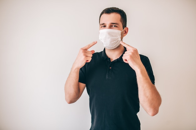 Jonge zieke man geïsoleerd over muur. Man in zwart shirt dragen medische bescherming masker. Waarschijnlijk zieke zieke wijzen erop.