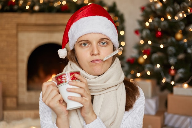 Jonge zieke vrouw in kerstmuts, verpakt in sjaal