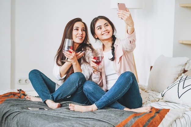 Jonge zorgeloze brunette meisjes vrienden in casual met glazen wijn nemen selfie en plezier samen op huisfeest