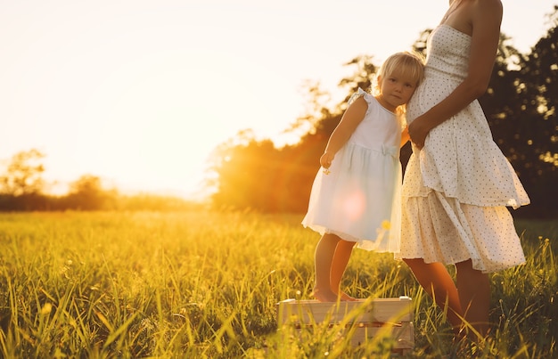 Jonge zwangere moeder en dochter in jurk op de natuur buitenshuis Zwangere vrouw en kind in de weide