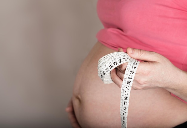 Jonge zwangere tussen 30 en 35 jaar oude vrouw houdt meetband voor haar buik. Detailopname