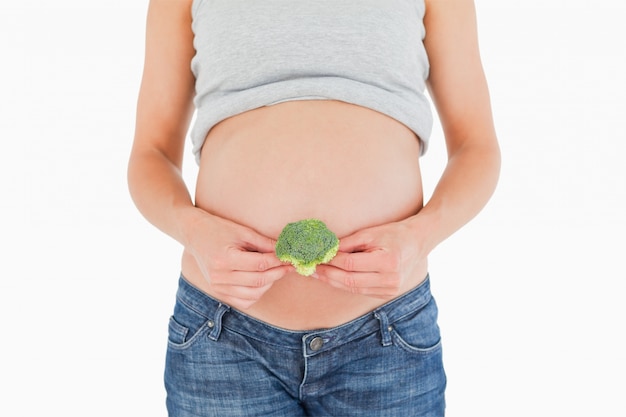 Jonge zwangere vrouw die broccoli houdt terwijl status