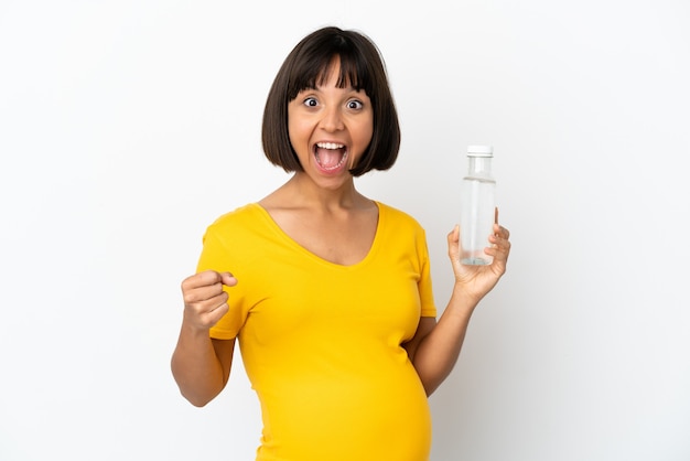 Jonge zwangere vrouw die een fles water houdt die op witte achtergrond wordt geïsoleerd en een overwinning in winnaarspositie viert